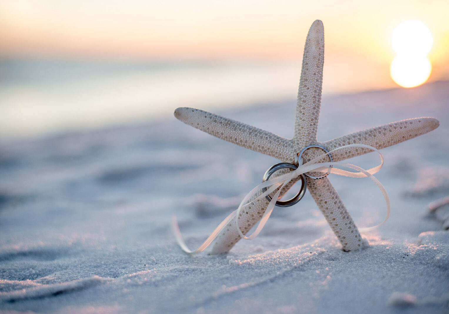 Wedding Rings tied to a Starfish Stuck in the Sand on the Beach with the Sunset in the Background